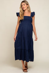 woman wearing a navy blue maternity dress with ruffled sleeves and a tiered skirt, showcasing her baby bump