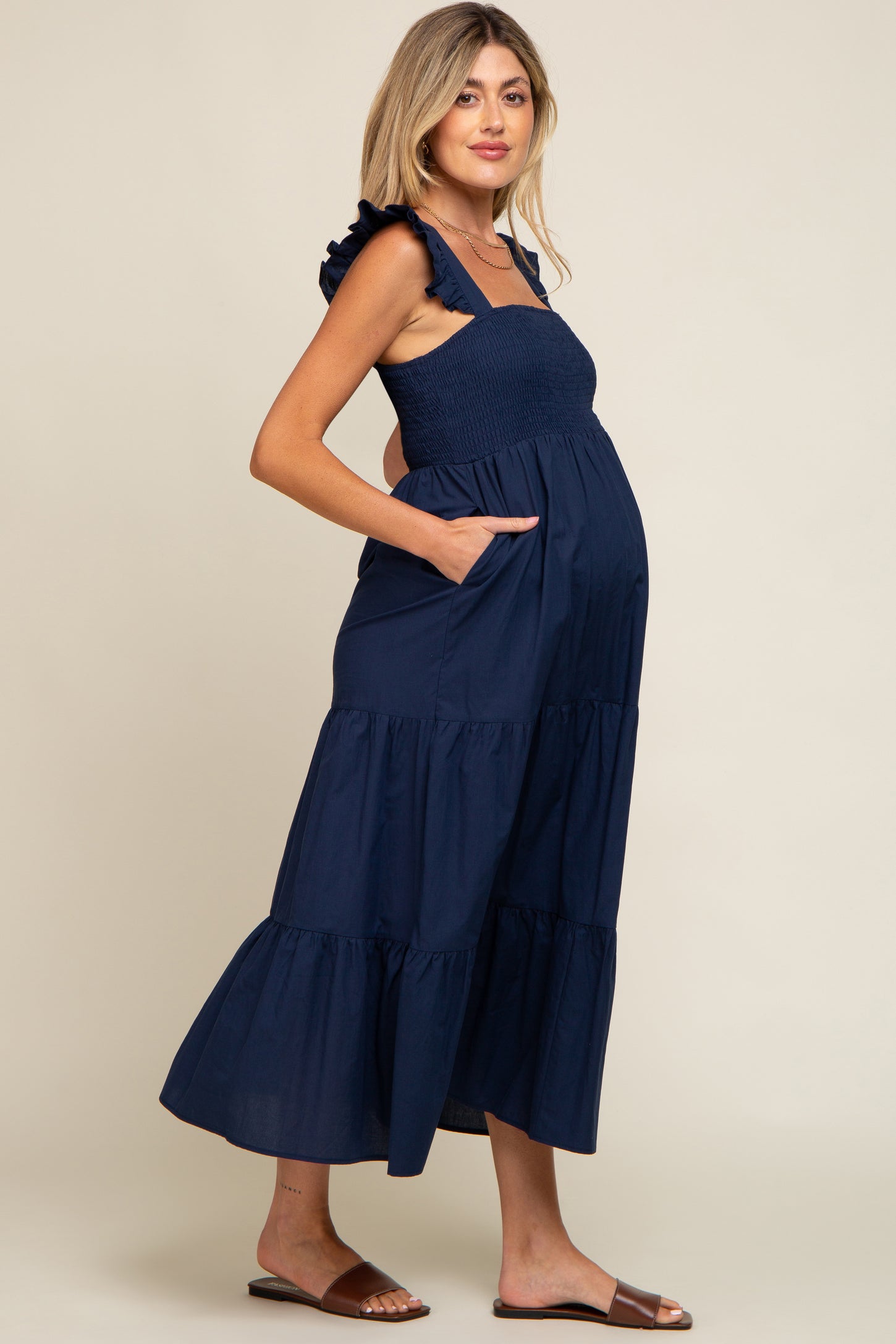 woman wearing a navy blue maternity maxi dress with ruffled straps and pockets, showcasing her baby bump