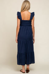 woman wearing a navy blue maternity maxi dress with ruffled straps and a smocked bodice, showing her back