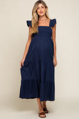 woman wearing a navy blue maternity maxi dress with ruffled sleeves and a tiered skirt, showcasing her baby bump