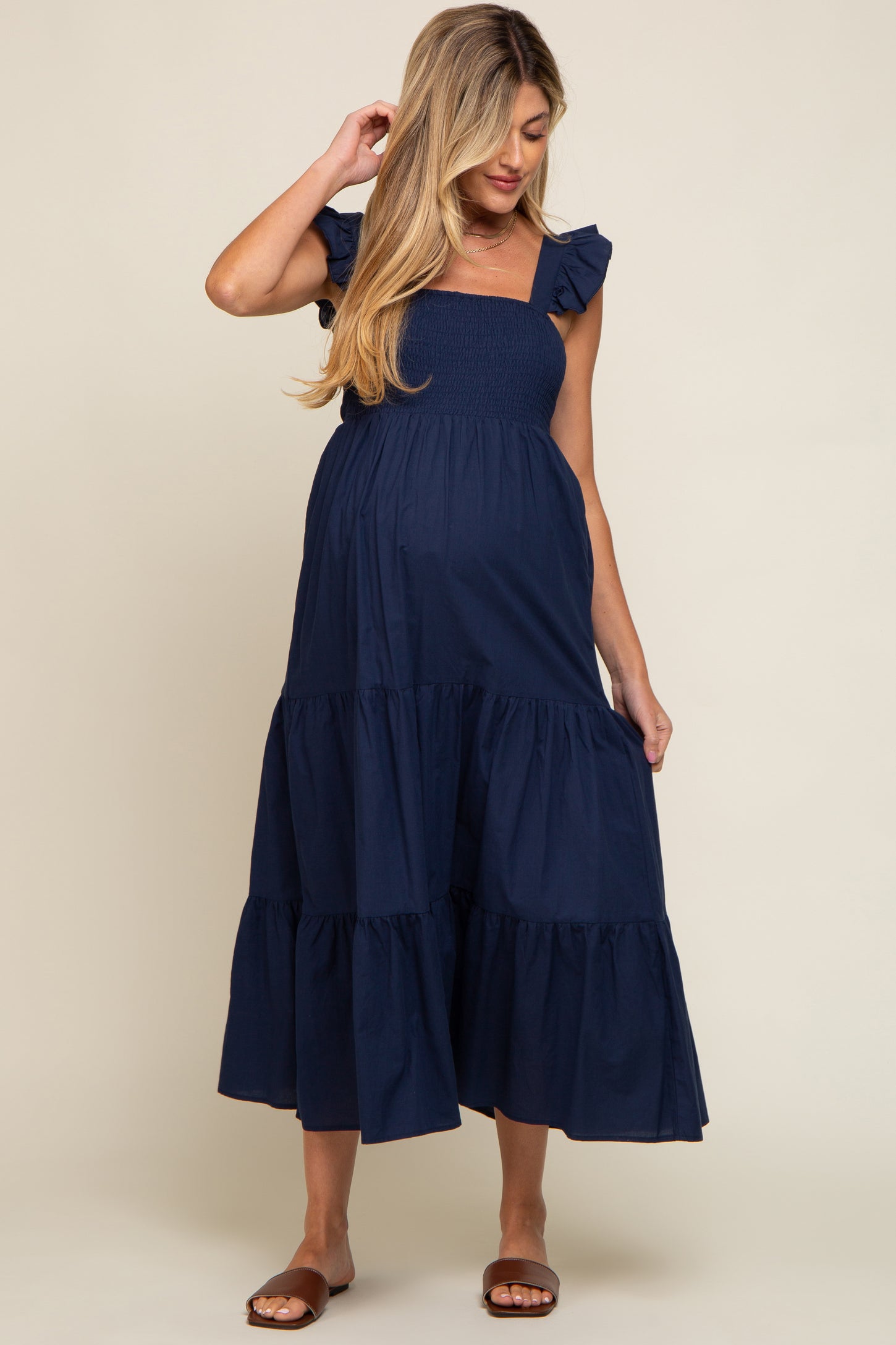 woman wearing a navy blue maternity dress with ruffled sleeves and a tiered skirt, showcasing a baby bump
