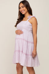 Smiling pregnant woman wearing a light purple tiered maternity dress with tie straps and lace trim.