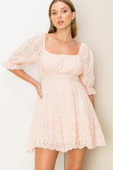 woman wearing a light pink eyelet mini dress with puff sleeves and a square neckline