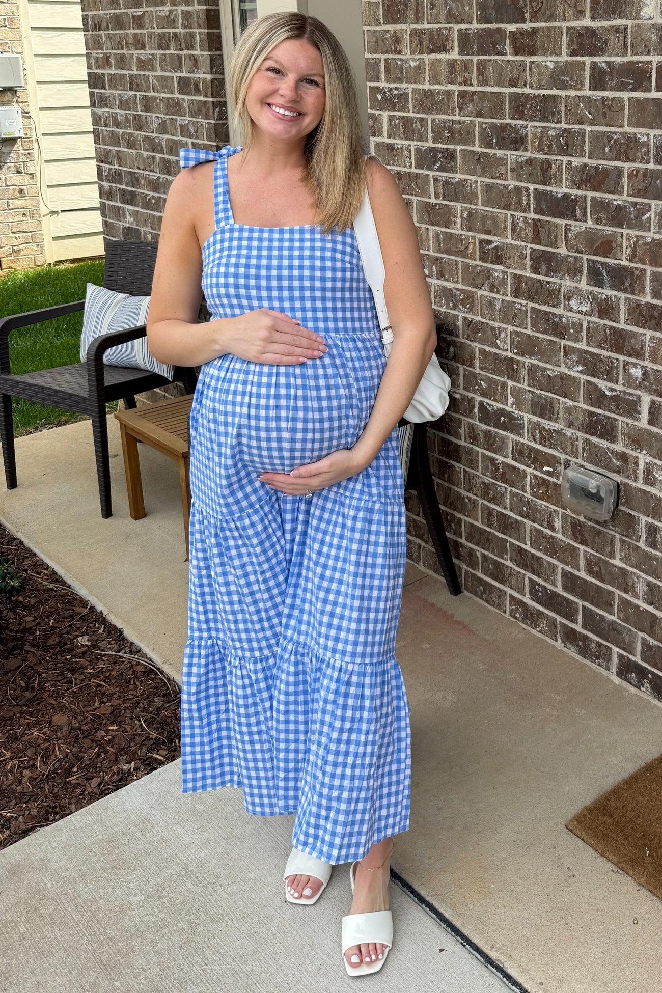 woman wearing a blue and white gingham maternity maxi dress with a tiered skirt, holding her baby bump