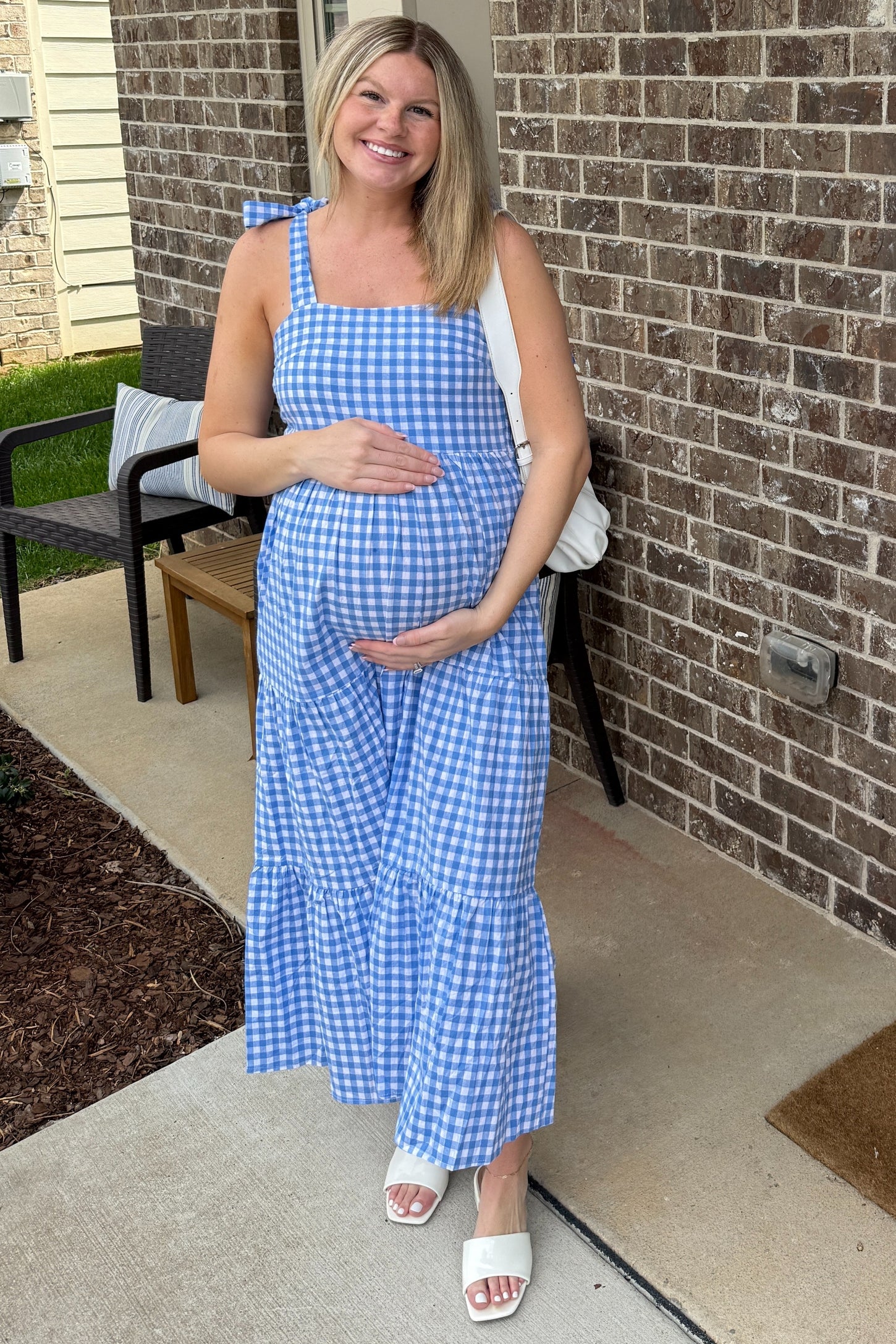 woman wearing a blue and white gingham maternity maxi dress with a tiered skirt, holding her baby bump