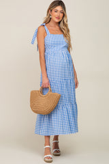woman wearing a blue and white gingham maternity dress with a tiered design and holding a straw bag