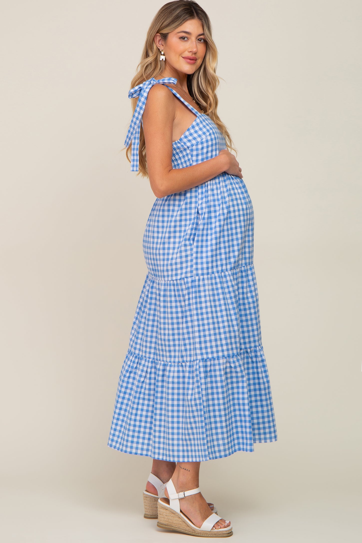 woman wearing a blue and white gingham maternity dress with tie straps and a flowing skirt, showing her baby bump