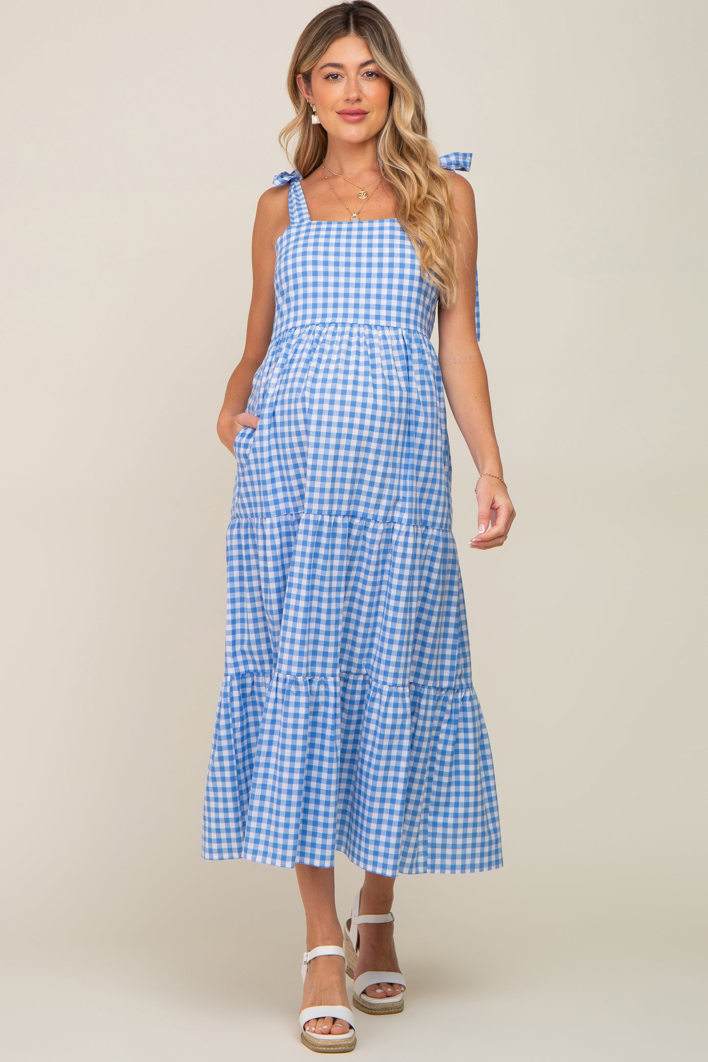 woman wearing a blue and white gingham maternity dress with tie straps and a tiered skirt, showing her baby bump