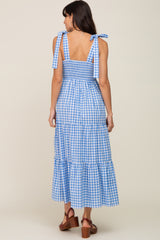 woman wearing a blue and white gingham maxi dress with tie shoulder straps and a tiered skirt detail