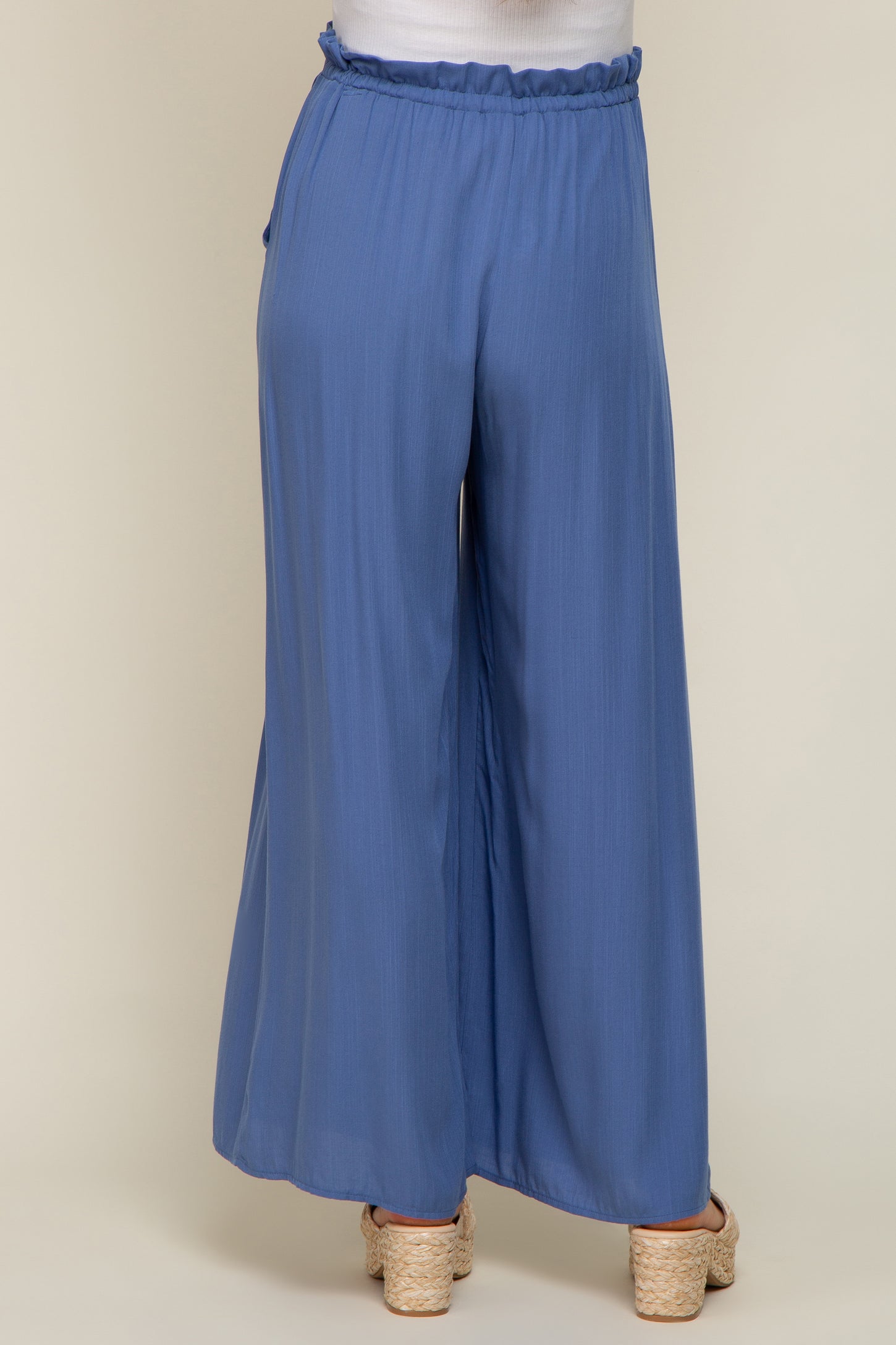back view of woman wearing blue wide leg pants with elastic paperbag waist and woven wedge sandals
