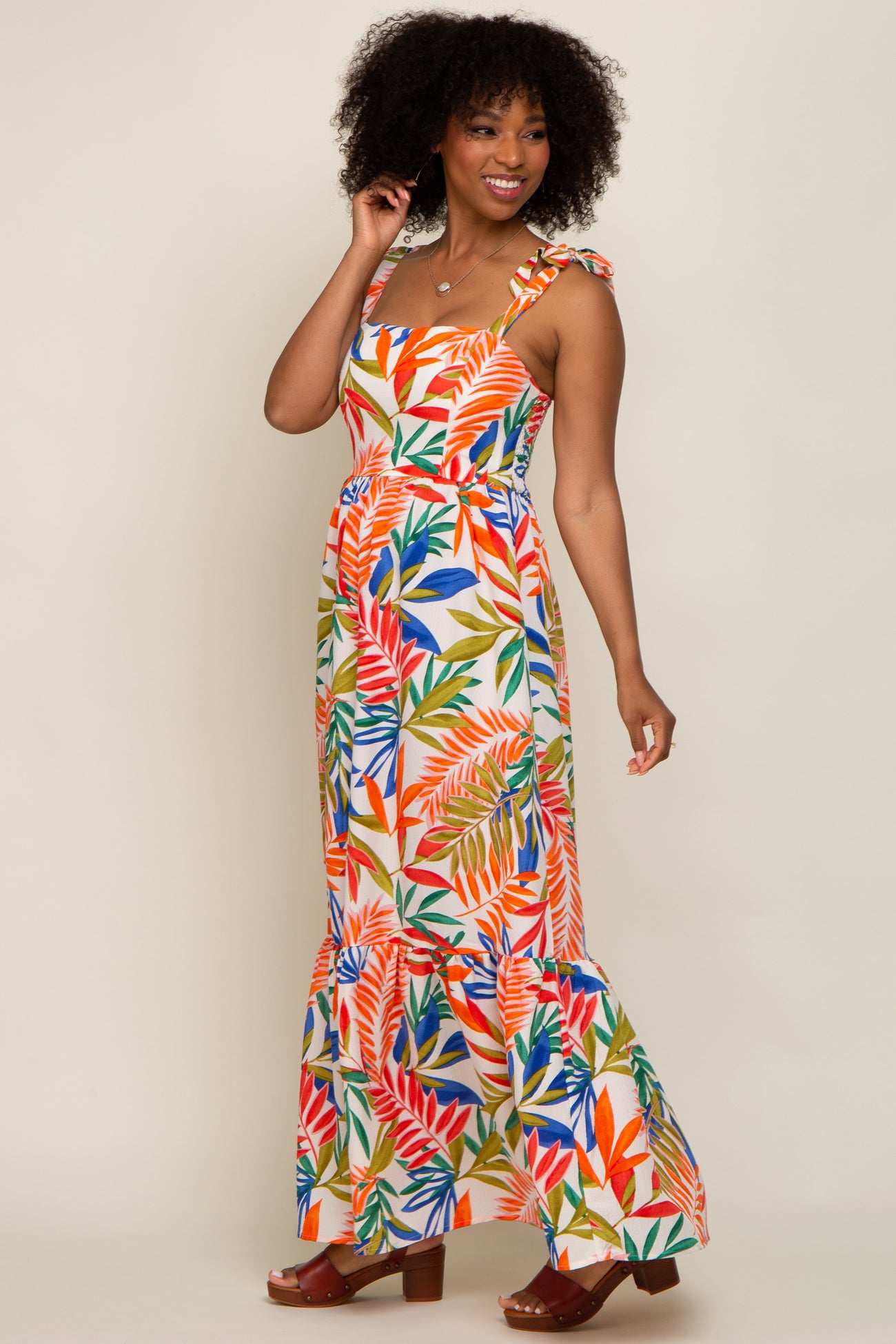 woman wearing a colorful tropical print maxi dress with ruffled straps and a flared hem