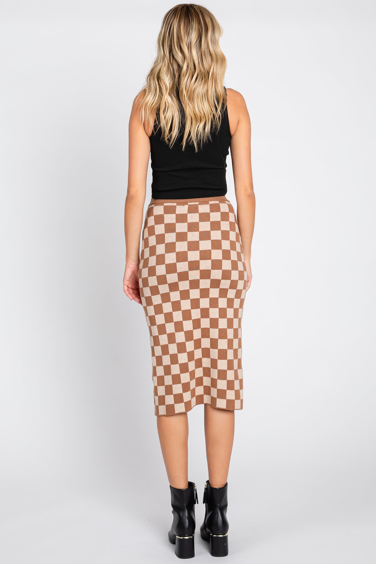 woman wearing a black sleeveless top and a brown and cream checkered mid-length skirt, viewed from the back