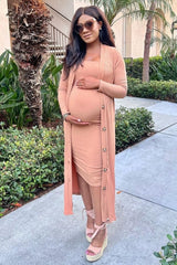 woman wearing a light pink maternity dress with a matching long cardigan, highlighting her baby bump, standing outdoors