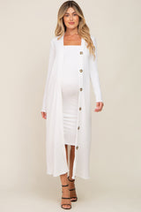 woman wearing a white ribbed maternity duster over a fitted white maternity dress, showing her baby bump
