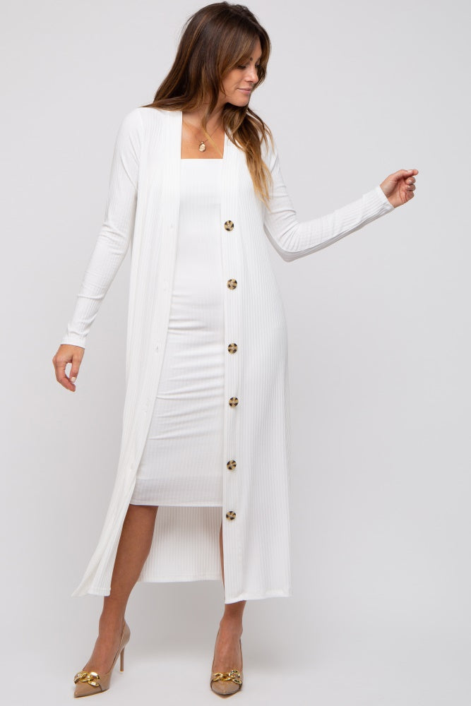woman wearing a white long sleeve cardigan with button details over a white bodycon dress and gold heels