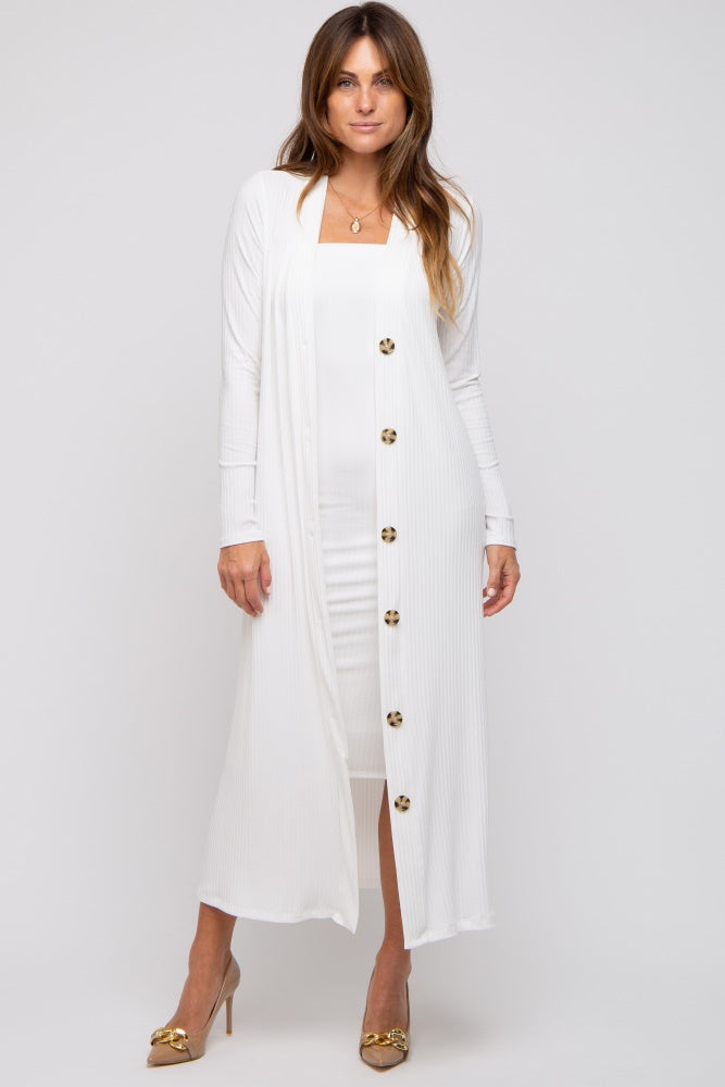 woman wearing a long white cardigan over a fitted white dress, standing in a relaxed pose with buttons down the front
