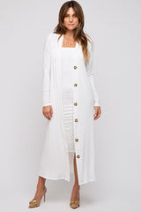 woman wearing a long white cardigan over a fitted white dress, standing in a relaxed pose with buttons down the front