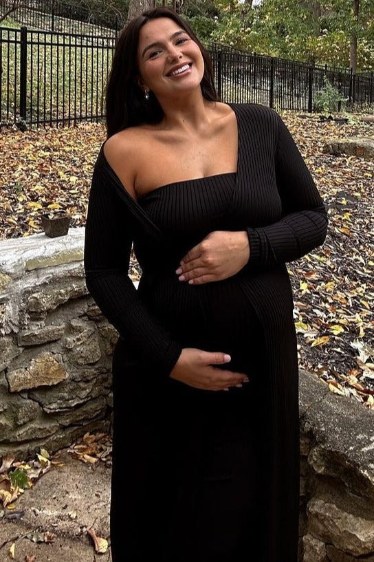 woman wearing a black ribbed off-the-shoulder maternity dress and holding her baby bump