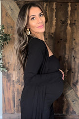 woman wearing a black maternity dress and cardigan, gently holding her baby bump