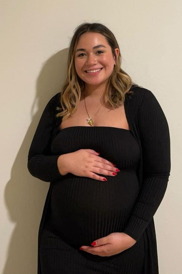 woman wearing a black ribbed maternity dress, holding her baby bump and smiling