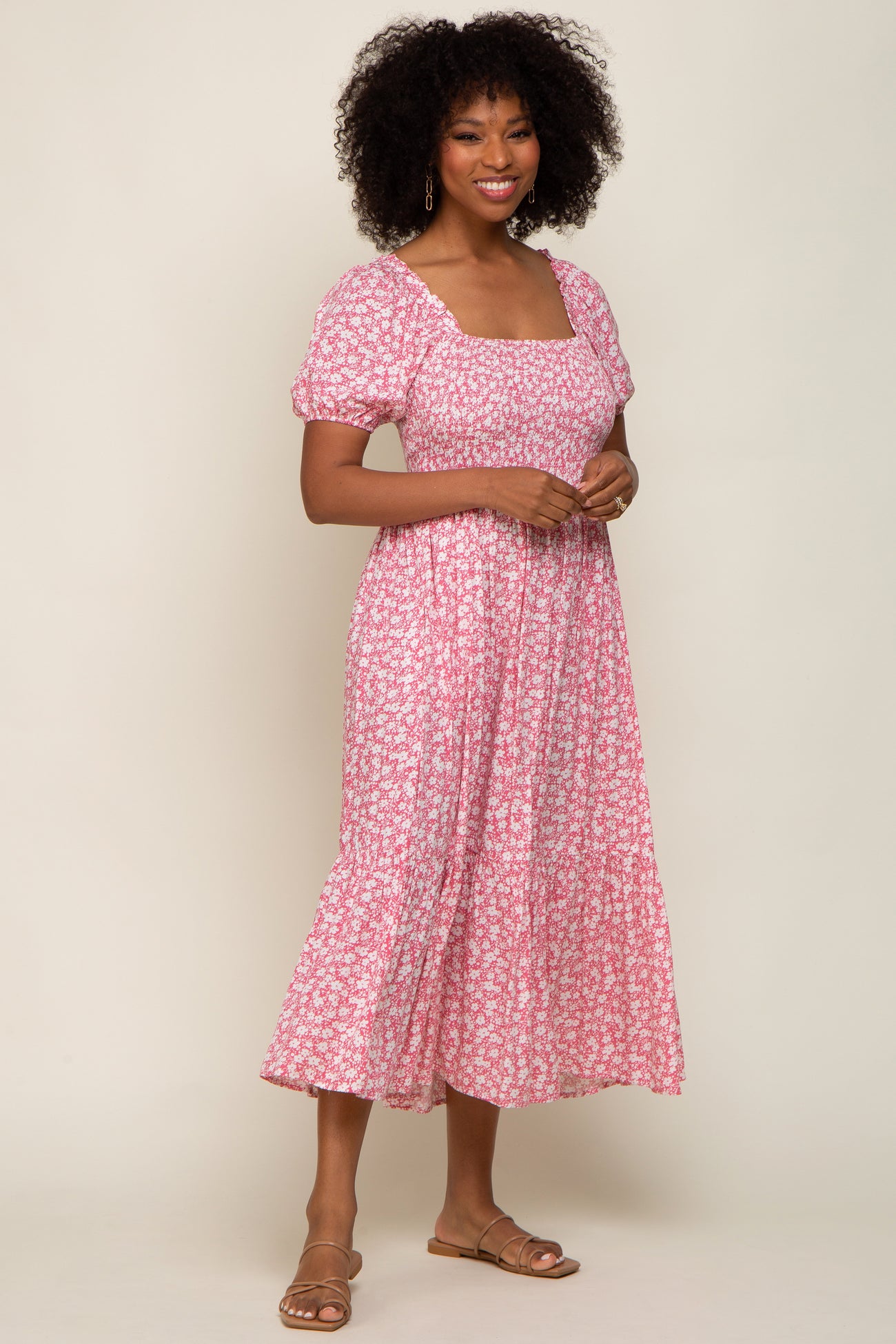 woman wearing a pink floral midi dress with puff sleeves and a square neckline, standing and smiling