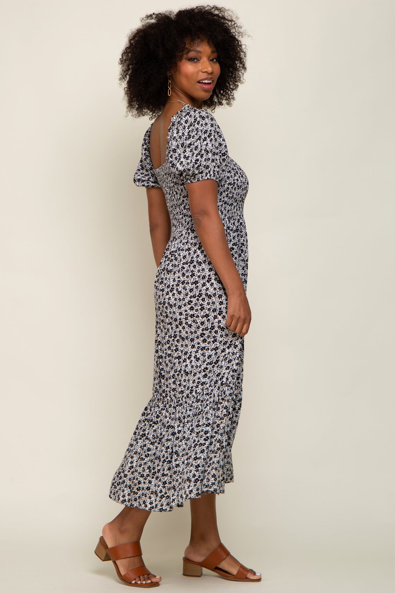 woman wearing a black and white floral midi dress with short puff sleeves and a ruffled hem, standing sideways