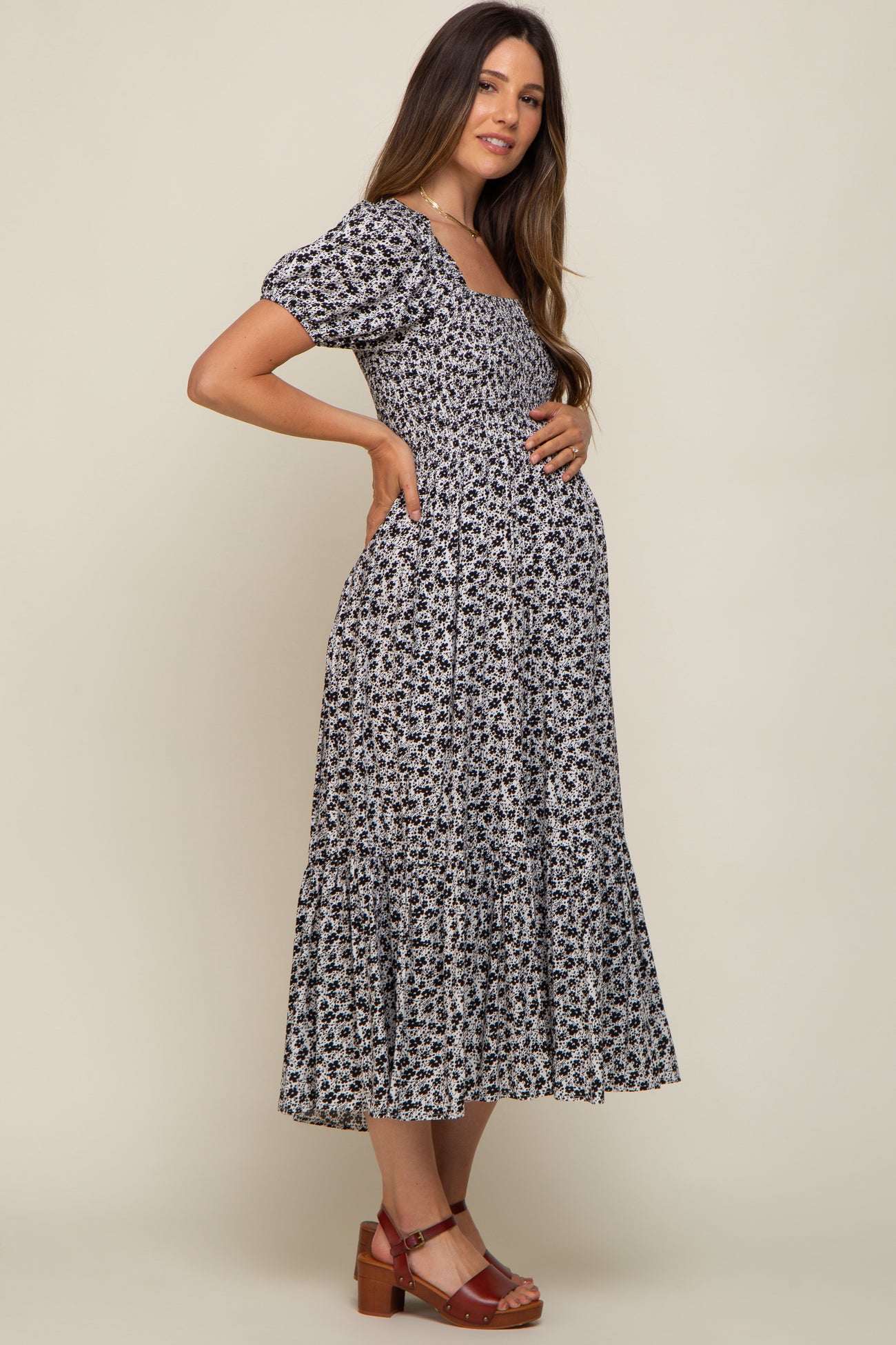 woman wearing a black floral maternity dress with short sleeves and a tiered skirt, holding her baby bump