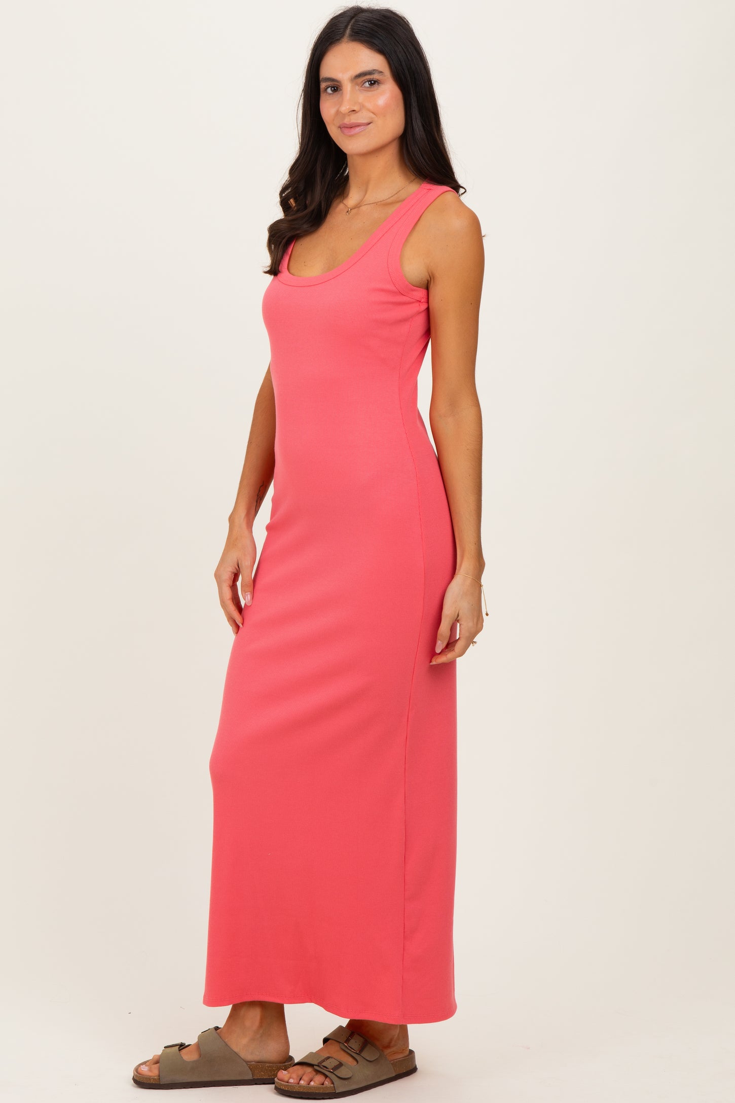 woman wearing a coral sleeveless maxi dress with a fitted silhouette and side slit, standing in profile