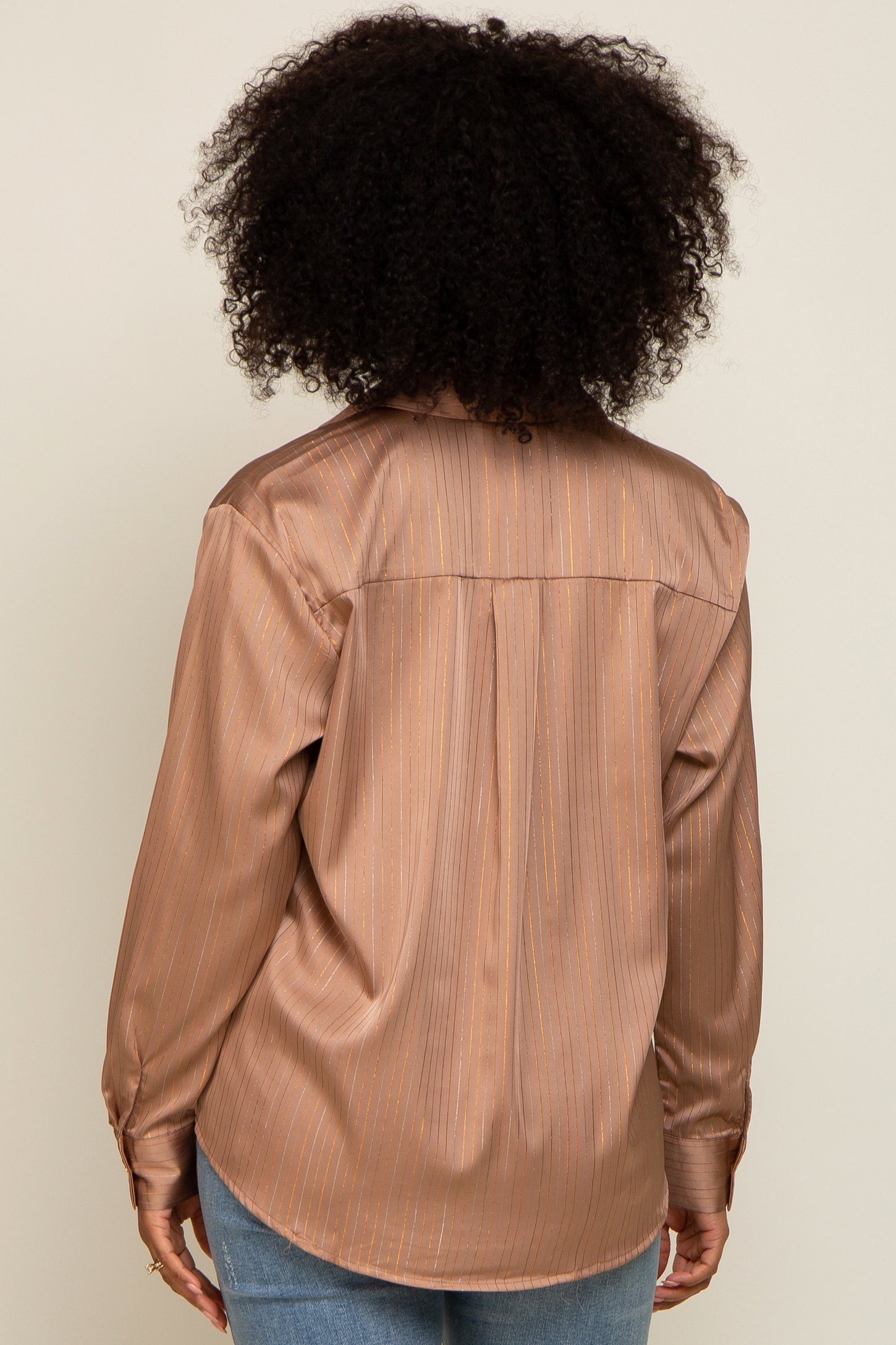 Back view of a person with curly hair wearing a bronze satin button-down shirt with gold vertical stripes.
