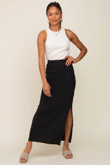 woman wearing a white ribbed tank top and a black maxi skirt with a side slit, posing with one hand on her hip