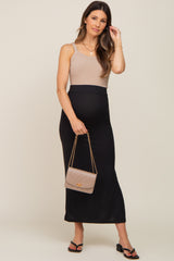 woman wearing a beige maternity tank top and a black ribbed midi skirt, holding a beige handbag and showing her baby bump