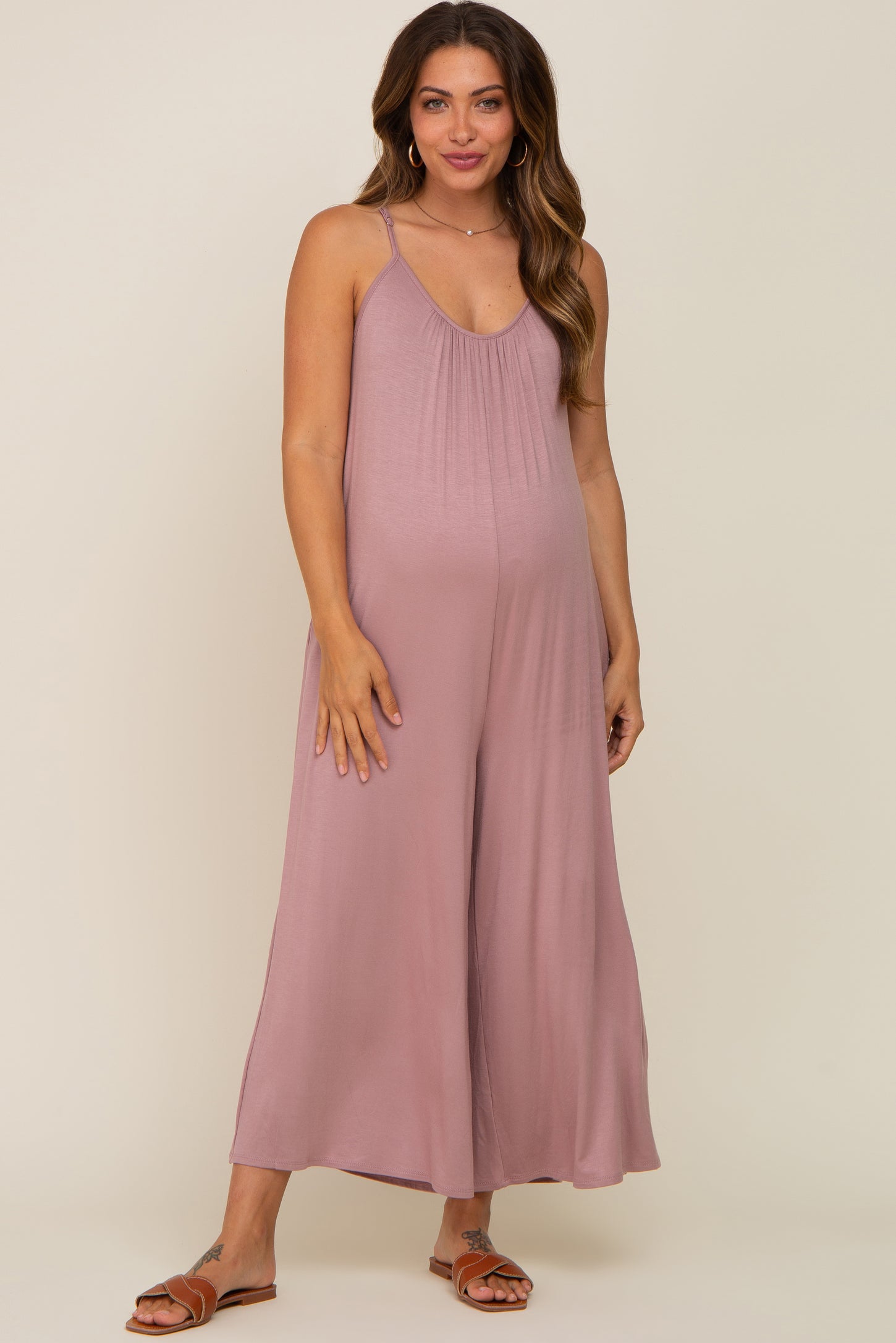 woman wearing a mauve maternity jumpsuit with a pleated front and spaghetti straps, showing her baby bump