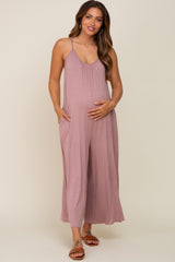 woman wearing a mauve sleeveless maternity jumpsuit with pockets and a visible baby bump, standing and smiling