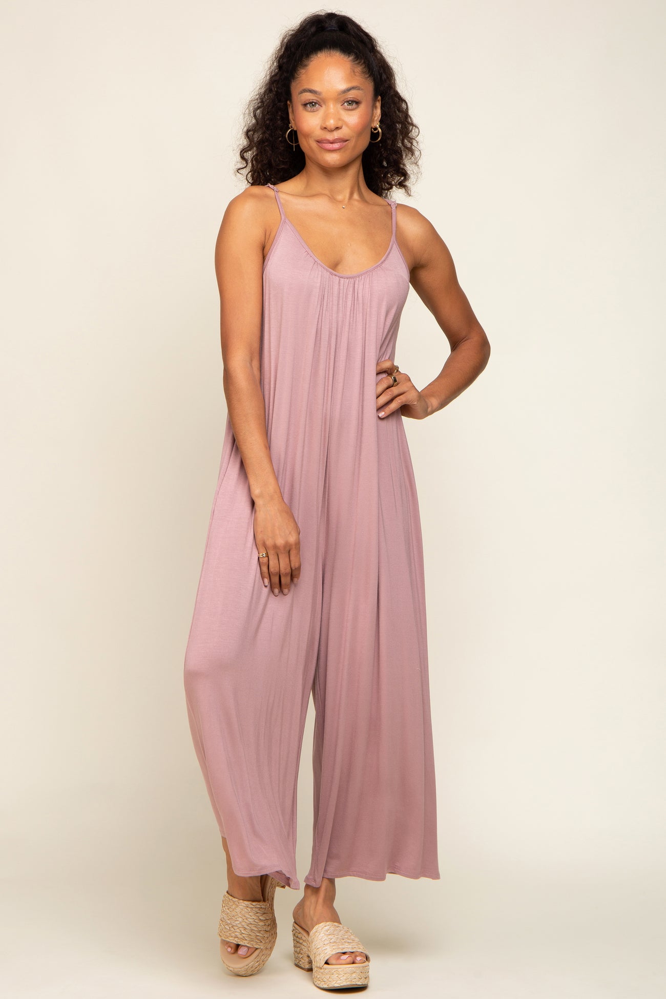 Woman wearing a mauve sleeveless wide-leg jumpsuit and woven platform sandals against a neutral background