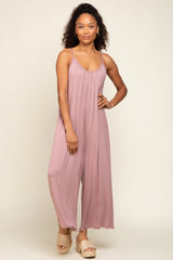 Woman wearing a mauve sleeveless wide-leg jumpsuit and woven platform sandals against a neutral background