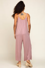 woman wearing a mauve sleeveless jumpsuit with loose fitting legs and a strappy back, standing with her back to the camera