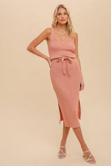 woman wearing a ribbed midi dress in blush pink with a tie waist and side slits, styled with strappy sandals
