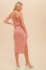 woman wearing a pink ribbed midi dress with side slits and spaghetti straps, standing with her back facing the camera