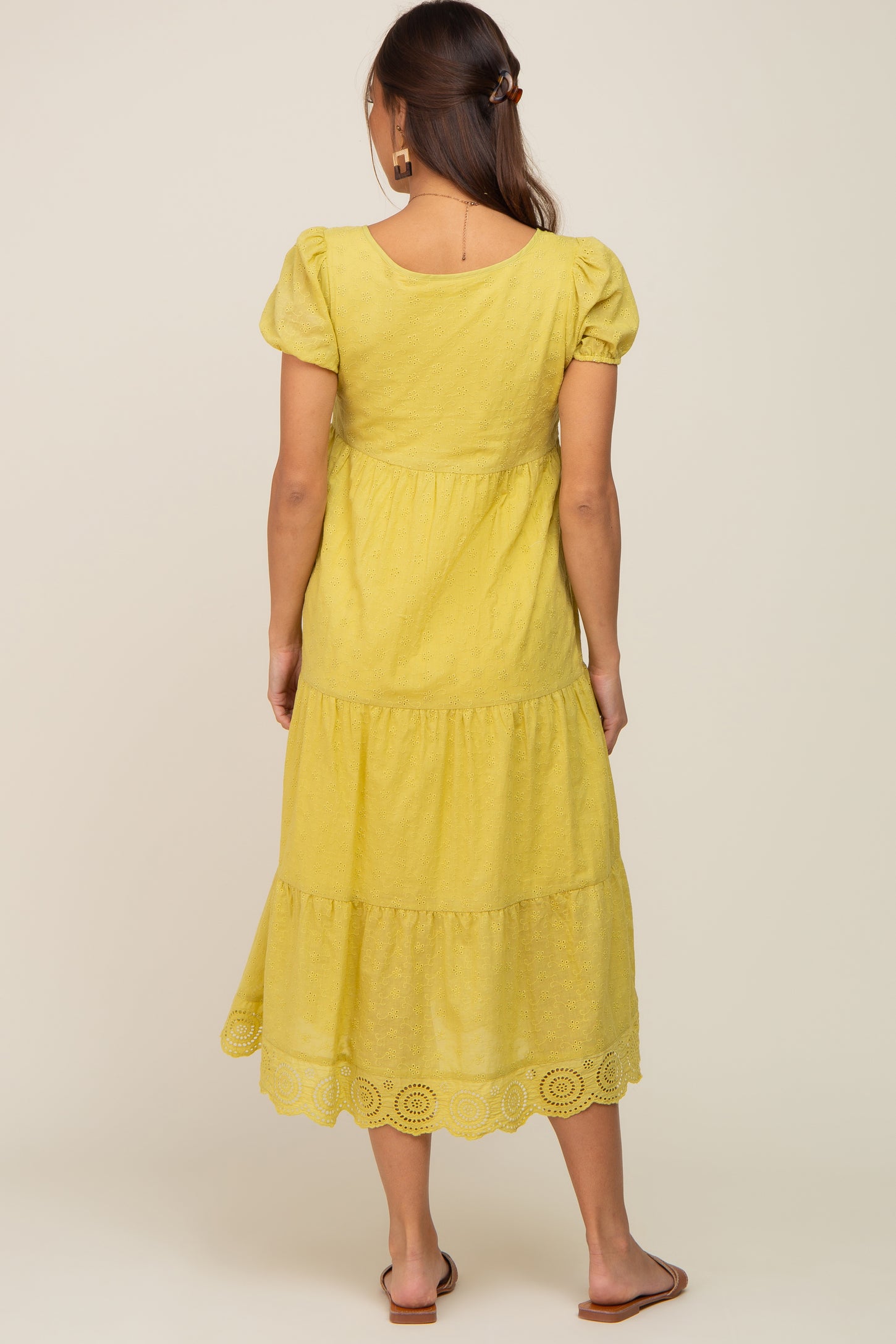 Back view of a woman wearing a yellow eyelet tiered midi dress with puff sleeves and scalloped hem