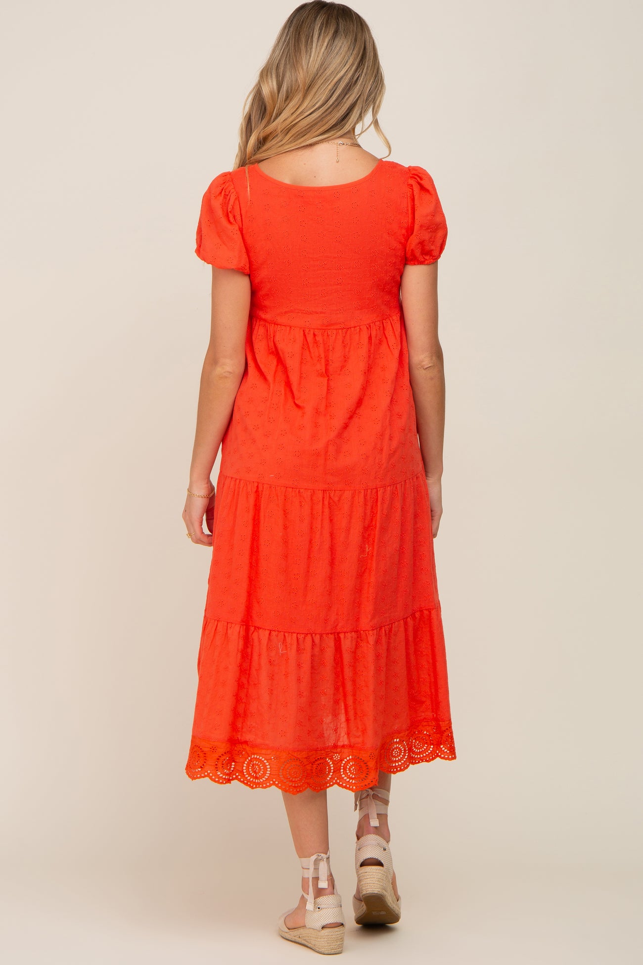Back view of a woman wearing a red tiered eyelet midi dress with puff sleeves and espadrille wedges