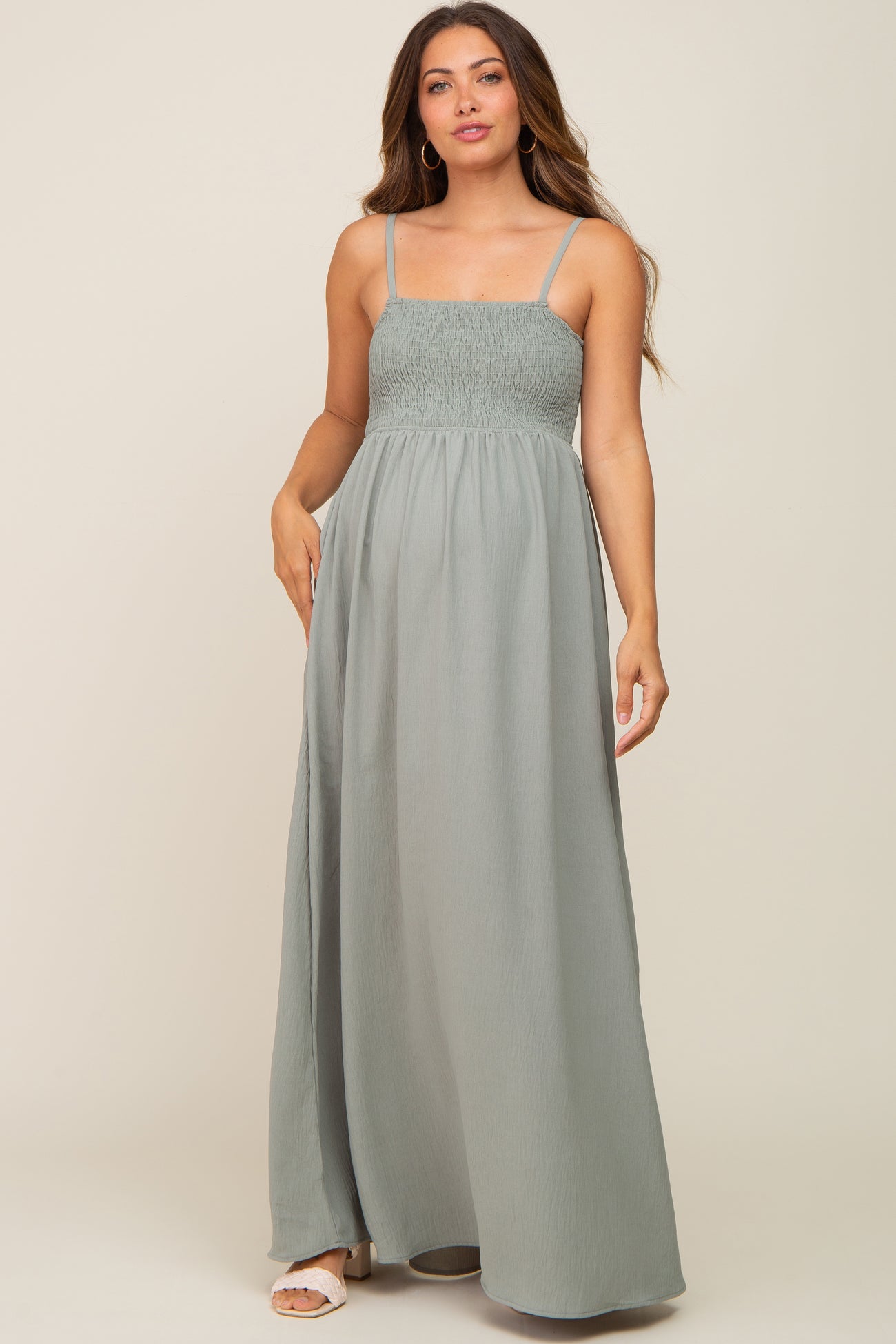 woman wearing a sage green smocked maternity maxi dress with spaghetti straps