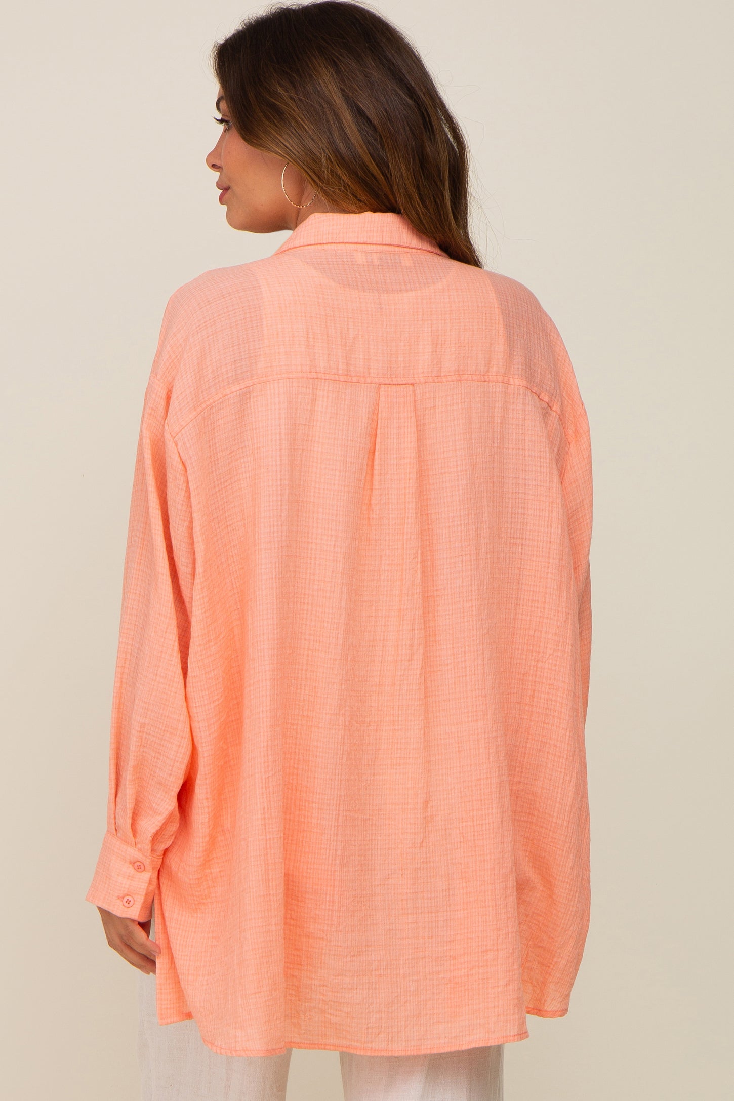 Back view of a woman wearing an oversized peach button-down linen shirt with long sleeves and a collar