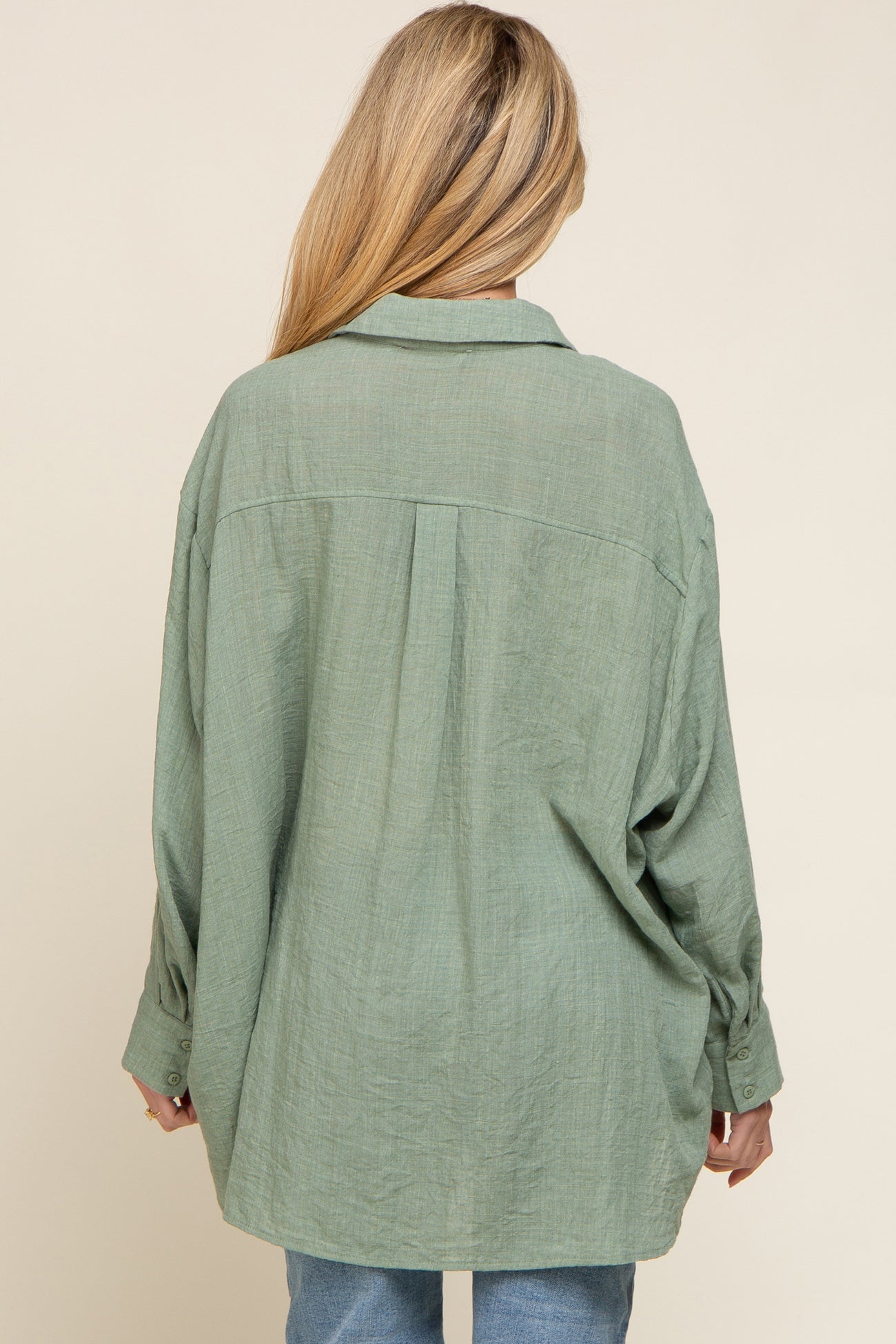 back view of a woman wearing an oversized sage green button-down linen shirt with a pleated back yoke