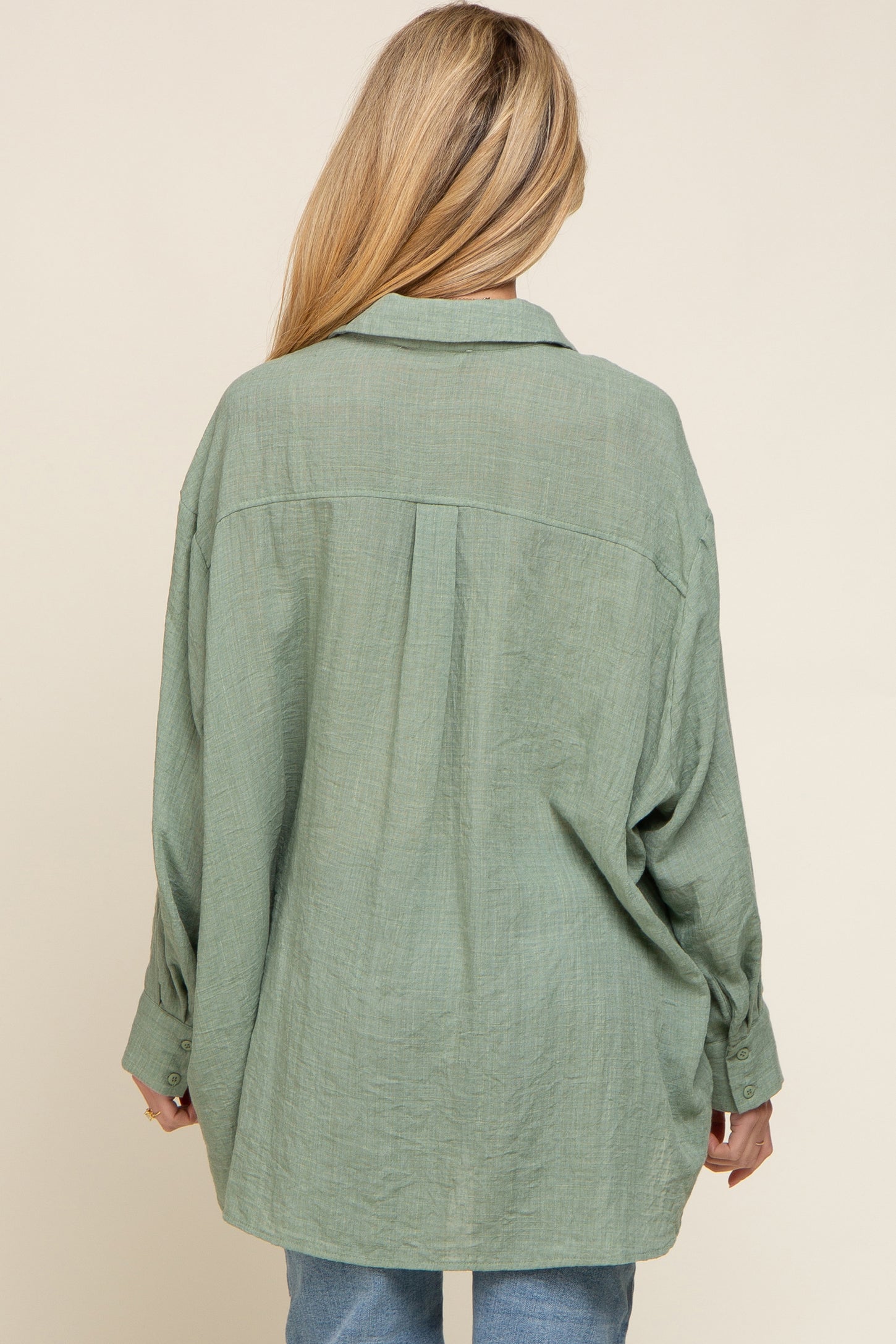 back view of a woman wearing an oversized sage green button-down linen shirt with a pleated back yoke