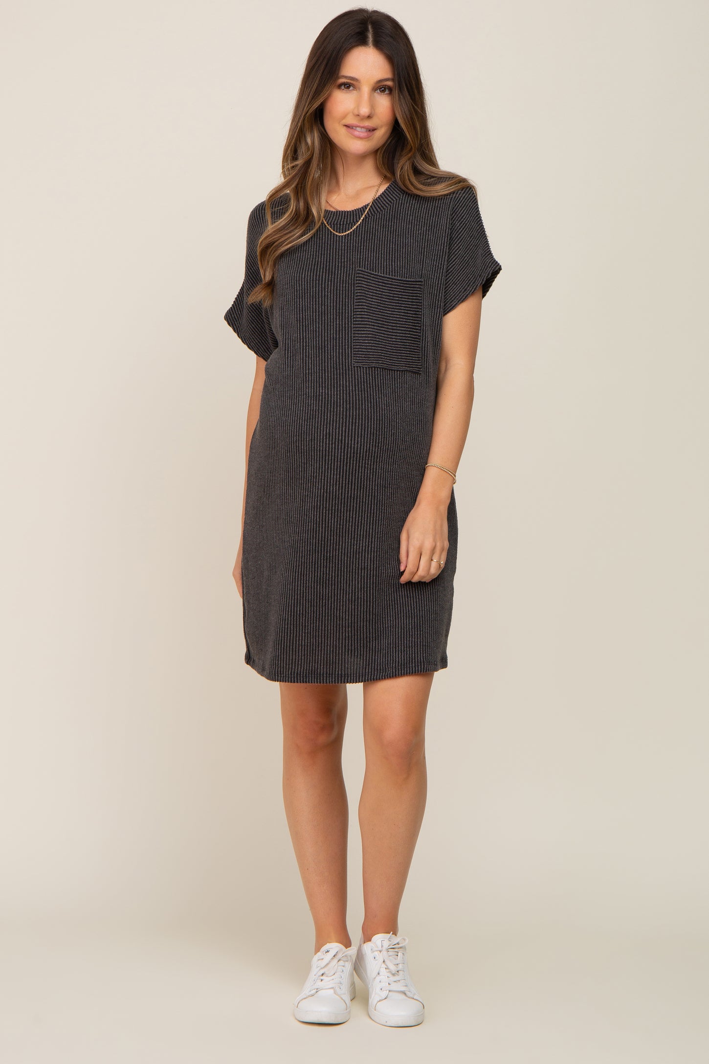 woman wearing a black striped maternity dress with a pocket and short sleeves, standing in white sneakers