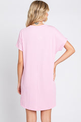 Back view of a woman wearing a light pink short sleeve ribbed knit mini dress against a white background