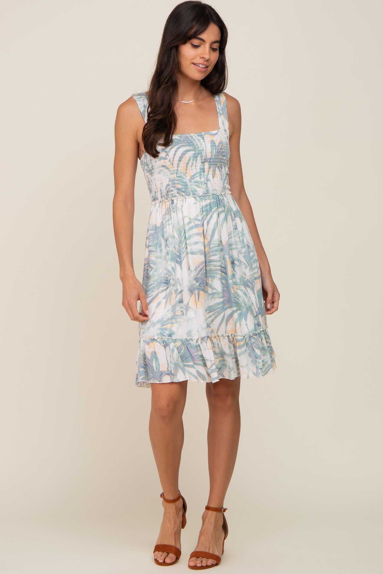woman wearing a tropical palm print smocked maternity dress with ruffle hem and brown sandals