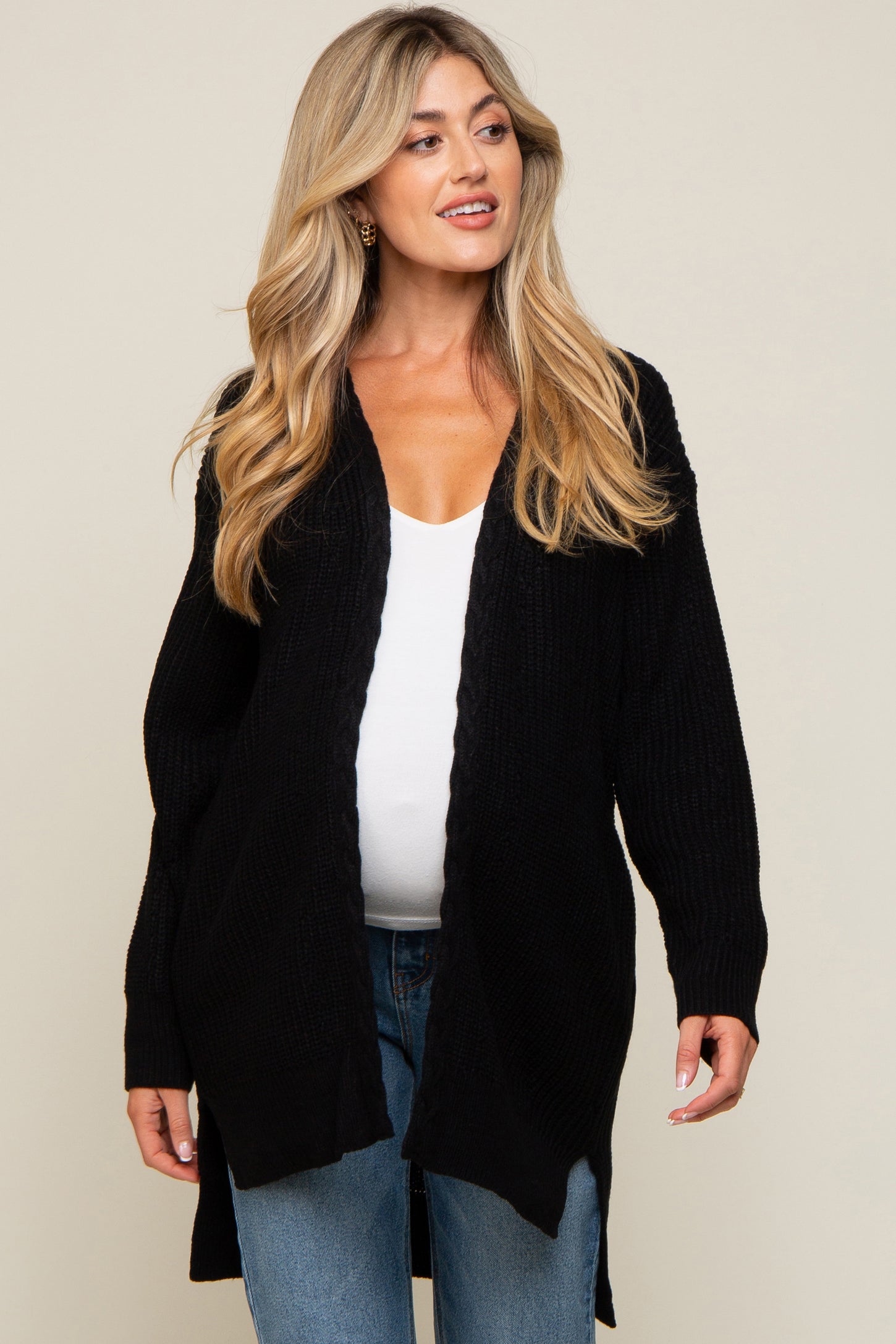 pregnant woman wearing a black open-front knit cardigan over a white top and blue jeans