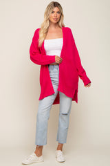 woman wearing a long hot pink knit cardigan over a white crop top and distressed light wash jeans