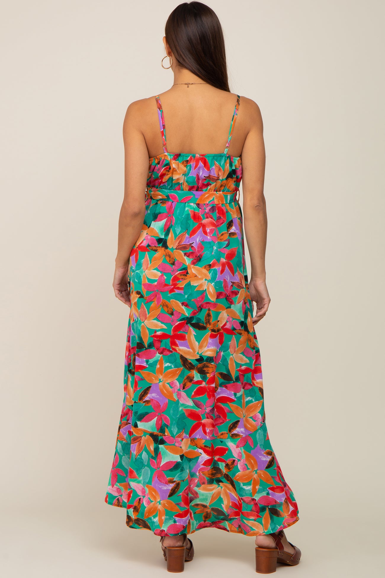 Back view of a woman wearing a green floral print maxi dress with spaghetti straps and a tiered skirt